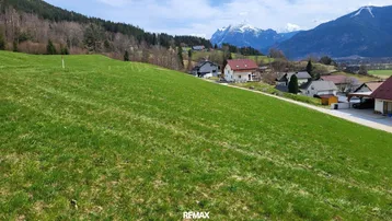 Weitläufiges grünes Grundstück mit Blick auf die umliegende Berglandschaft und einige Häuser.