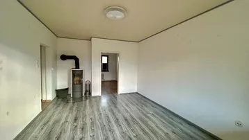 Geräumiges Wohnzimmer mit grauem Laminatboden und einem gemütlichen Holzofen in der Ecke.