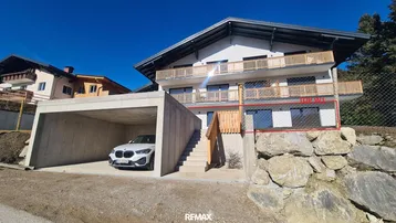 Modernes Gebäude mit mehreren Balkonen, Carport und Bergblick unter blauem Himmel.