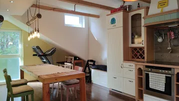 Helle Wohnküche im Dachgeschoss mit sichtbaren Holzbalken, integriertem Essbereich und modernen Einbaugeräten.