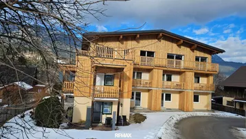 Modernes Gebäude mit Holzfassade und Balkonen in verschneiter Berglandschaft.
