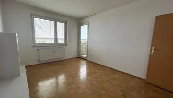 Geräumiges, helles Zimmer mit Parkettboden, Fenster und Zugang zu einem französischen Balkon.