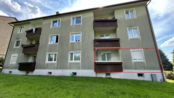 Mehrfamilienhaus mit mehreren Balkonen und einer grünen Rasenfläche davor unter blauem Himmel.