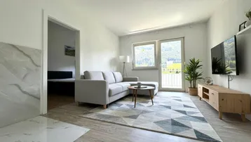 Helles Wohnzimmer mit modernem Sofa, Teppich und Bergblick durch große Fenster mit Balkonzugang.