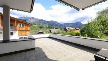 Große gepflasterte Terrasse mit Markise und beeindruckendem Bergblick in alpiner Umgebung.