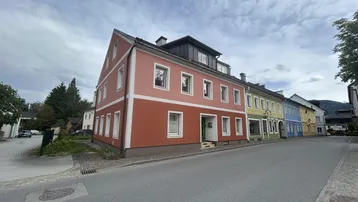 Mehrstöckiges Gebäude mit markanter rot-oranger Fassade an einer Wohnstraße unter bewölktem Himmel.
