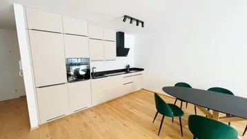Moderne, offene Küche mit hellen Schränken, dunkler Arbeitsplatte und Essbereich mit Holzboden.