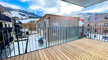 Geräumiger Balkon mit Holzboden und Blick auf die verschneite Berglandschaft und Baustelle.