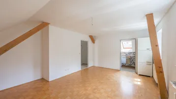 Helles, leeres Zimmer im Dachgeschoss mit Parkettboden und sichtbaren Holzbalken, bereit zur individuellen Gestaltung.