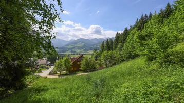 Panoramablick auf die umliegende Berglandschaft mit grünen Hügeln und vereinzelten Häusern unter blauem Himmel.