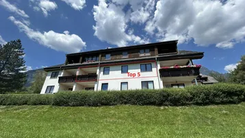 Mehrfamilienhaus mit Balkonen und gepflegter Grünfläche unter blauem Himmel.