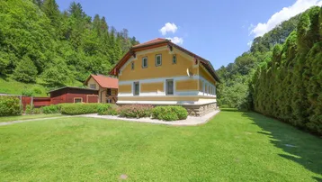Gelbes Landhaus mit rotem Dach und großem grünen Garten umgeben von Bäumen.