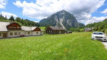 Ländliche Landschaft mit Häusern, grünen Wiesen und majestätischem Berg im Hintergrund unter blauem Himmel.
