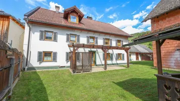 Großzügiger Gartenbereich mit Rasenfläche und einer Holzpergola vor dem Wohnhaus.