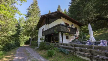 Traditionelles Landhaus in den Bergen mit einer kleinen, möblierten Terrasse und umgeben von viel Grün.