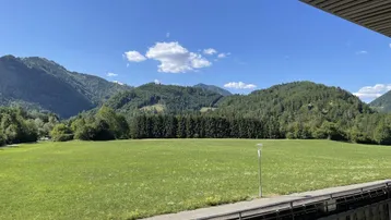 Weitläufiger Blick vom Balkon auf grüne Wiesen und bewaldete Berge.