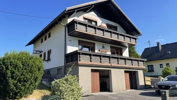 Traditionelles Einfamilienhaus mit zwei Balkonen und integrierter Garage in ländlicher Umgebung.
