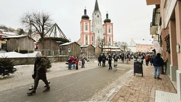 Eine belebte Straße im Winter mit einer historischen Kirche im Hintergrund und Menschen auf einem Markt.
