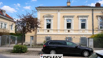 Historisches Gebäude mit gelber Fassade und klassischen Fenstern von der Straße aus gesehen.