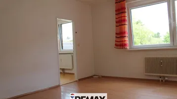 Helles, leeres Zimmer mit Laminatboden und Fenster mit Blick ins Grüne.
