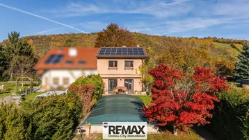 Hausfassade mit Solaranlage auf dem Dach, umgeben von einem gepflegten Garten mit Poolabdeckung.