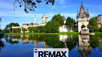 Malerisches Schloss am Seeufer mit Türmen und grüner Umgebung, spiegelt sich im Wasser wider.
