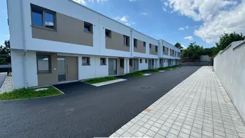 Moderne Reihenhäuser mit gepflastertem Gehweg und asphaltierter Zufahrt unter blauem Himmel.
