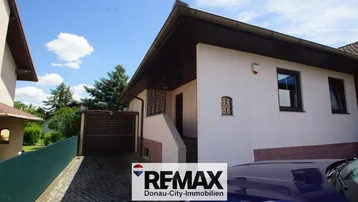 Außenansicht eines Einfamilienhauses mit gepflasterter Einfahrt und integrierter Garage unter blauem Himmel.