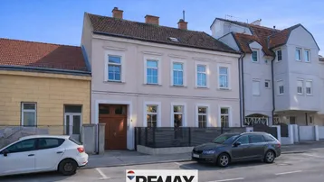 Historisches Gebäude mit heller Fassade und klassischen Fenstern an einer ruhigen Straße.