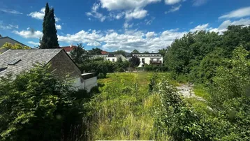 Blick auf ein unbebautes Grundstück mit viel Grün und umliegenden Gebäuden unter blauem Himmel.
