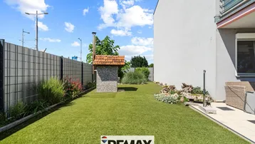 Gepflegter Gartenbereich mit Kunstrasen, Grillplatz und einer kleinen Steinhütte neben dem Haus.