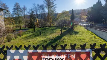 Blick auf das Grundstück mit grüner Wiese, Bäumen und einem Verkaufsbanner im Vordergrund.