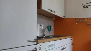 Kleine Einbauküche mit weißen Schränken, Herd und orangefarbenem Fliesenspiegel.