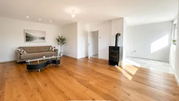 Helles Wohnzimmer mit Holzboden, gemütlichem Sofa und modernem Holzofen als Blickfang.