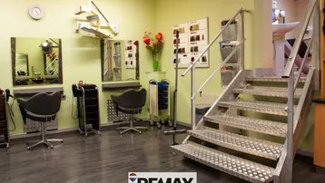 Innenansicht eines Friseursalons mit mehreren Styling-Stationen, Spiegeln und einer Metalltreppe zu einer oberen Ebene.