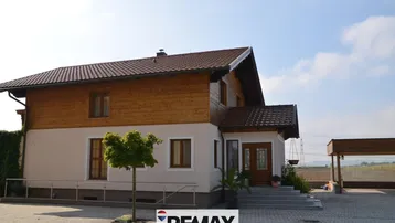 Freistehendes Einfamilienhaus mit Holzfassade, gepflasterter Einfahrt und Carport unter klarem Himmel.
