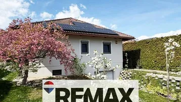 Hausfassade mit Solaranlage auf dem Dach, umgeben von blühenden Bäumen und einem gepflegten Garten.