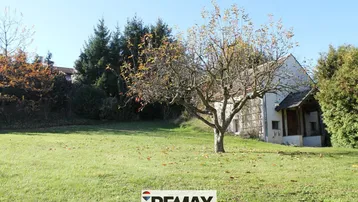Großer Gartenbereich mit Rasenfläche, einem Obstbaum und einem kleinen Nebengebäude im Hintergrund.