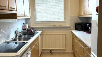 Helle Küche mit Holzschränken, Fliesenboden und Fenster über der Spüle.