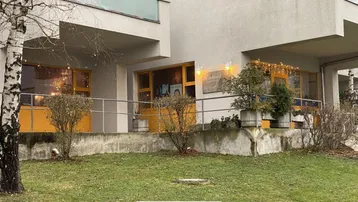 Ansicht der Gebäudefassade im Erdgeschoss mit kleinen Büschen und einer Rasenfläche davor.