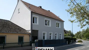Graue Fassade eines Wohnhauses mit Satteldach und Blick auf die Straße.