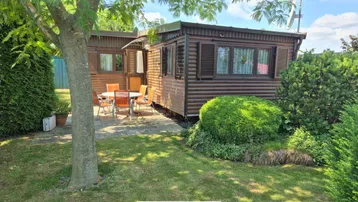 Gemütlicher Gartenbereich mit Terrasse und Gartenmöbeln vor dem Holzhaus unter blauem Himmel.