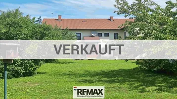Gepflegter Garten mit weitläufiger Rasenfläche und altem Baumbestand vor einem traditionellen Wohnhaus.