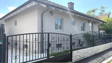 Vorderansicht des Hauses mit gepflegtem Vorgarten und schmiedeeisernem Zaun.