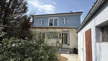 Rückansicht des Hauses mit einem Nebengebäude und einem gepflasterten Weg unter blauem Himmel.