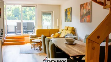 Heller Wohn- und Essbereich mit gelbem Sofa, Holztisch und Zugang zu einem Außenbereich.