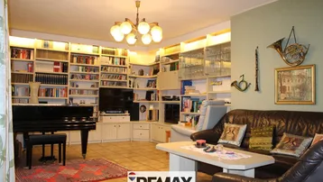 Gemütliches Wohnzimmer mit Ledersofa, Bücherregalen und einem Flügel, ideal für Musikliebhaber.
