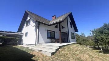 Freistehendes Einfamilienhaus mit Satteldach, weißer Fassade und einer Terrasse mit Sitzgelegenheiten.
