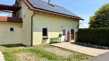 Gelbes Einfamilienhaus mit Solaranlage auf dem Dach und gepflegtem Vorgarten.