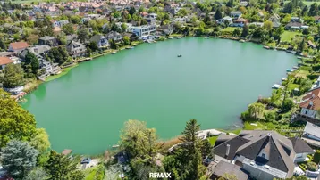 Luftaufnahme eines Sees umgeben von Wohnhäusern und viel Grün, mit einem weiten Blick über die Landschaft.